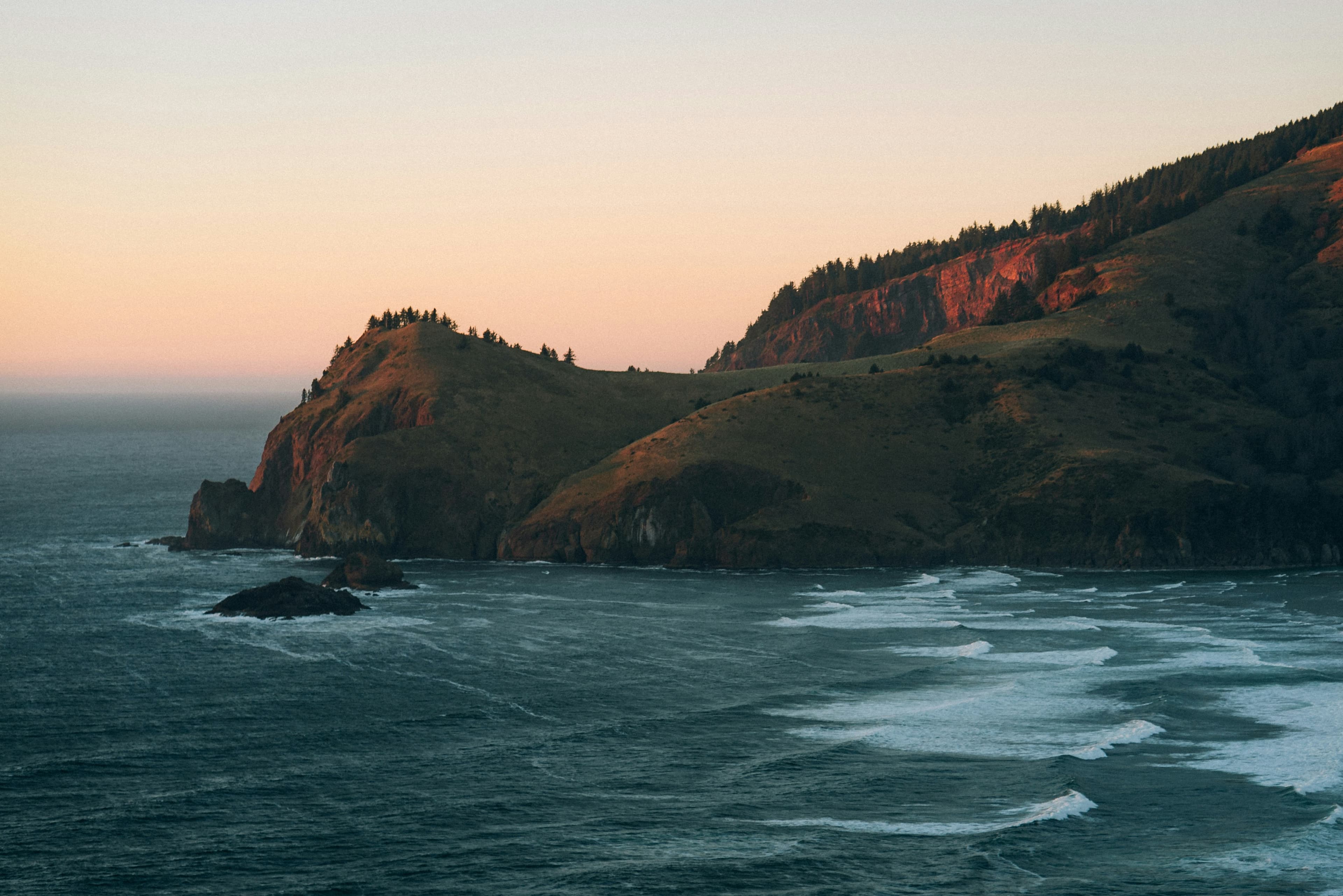 A quiet stretch of the Oregon coastline at dusk, muted cliffs meeting the Pacific